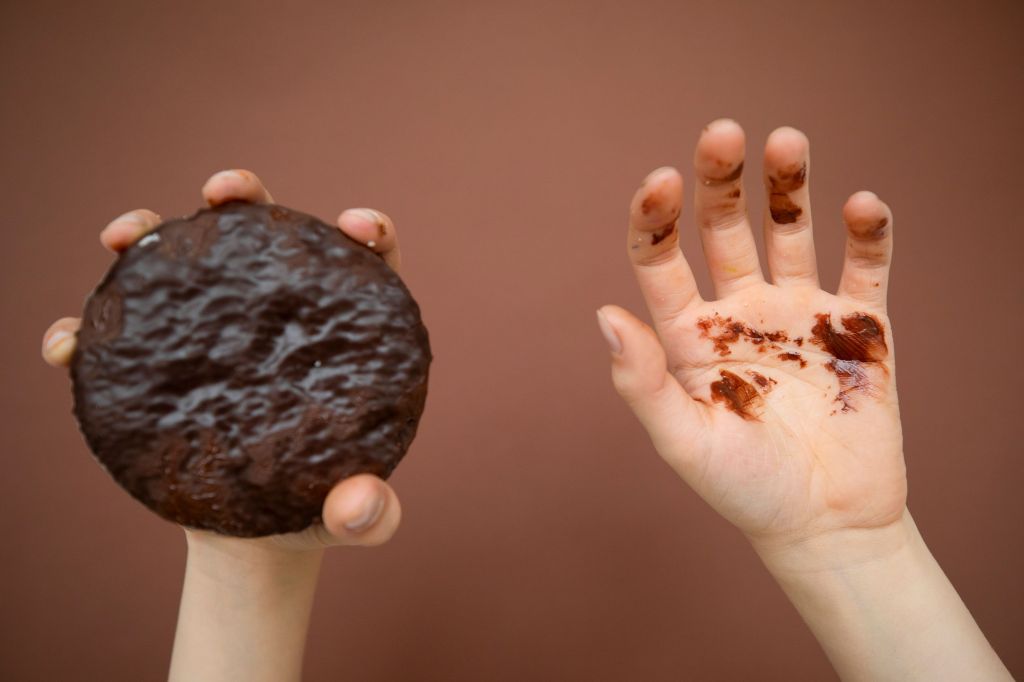 Mãos de criança sujas de chocolate segurando um biscoito coberto de chocolate, ilustrando a mentira infantil